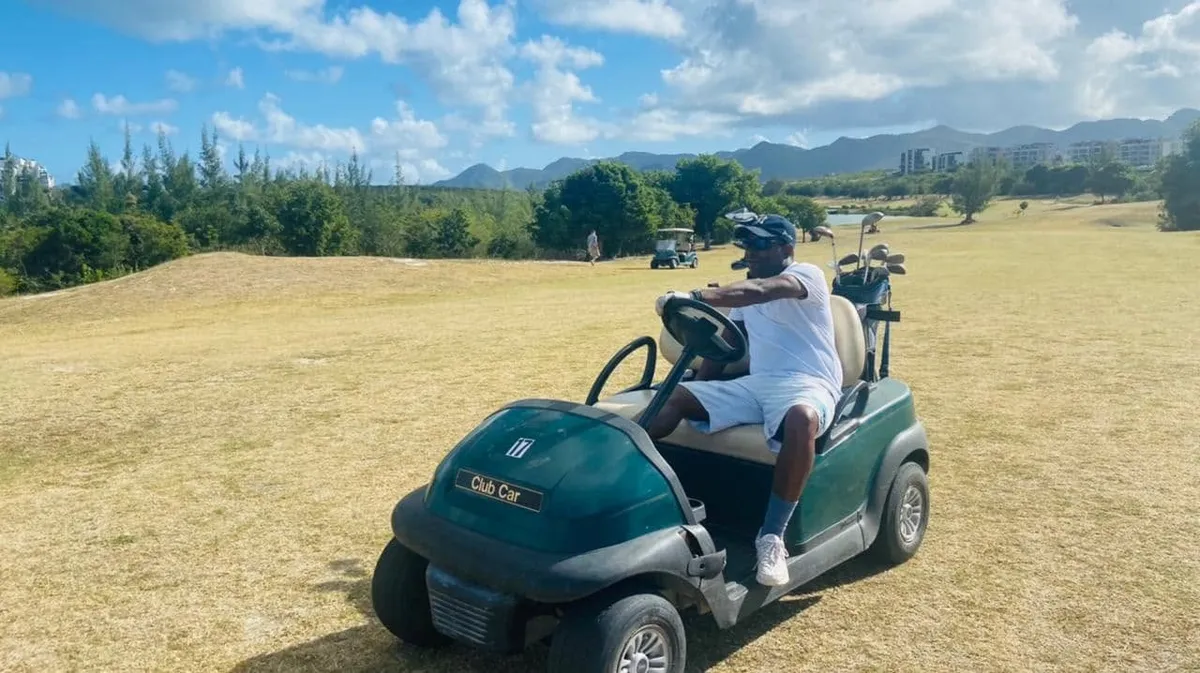 Sunquest broker driving a golf cart across a golf course, with green hills and high-rise buildings in the distance